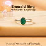 Gold ring with a green gemstone on a beige surface, with text about certification and branding.