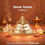 Shree Yantra Meru on a wooden surface with flowers and a lamp in the background