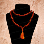 A double-strand rudraksha bead mala necklace with a tassel, displayed on a black mannequin bust against a textured beige background.