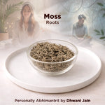 Glass bowl of dried moss on a white plate with a blurred background of two people and plants.