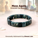 Moss Agate Emerald Cut Bracelet on a soft surface with a blurred background of people interacting.