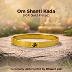 Gold bracelet with Om symbol on a stone surface, blurred background with flowers and light.