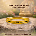 Gold bracelet with engraved text on a stone surface, with a blurred background of a statue and flowers.