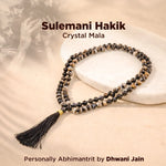 Crystal mala necklace with tassel on a textured surface, featuring 'Sulemani Hakik' branding.