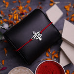 A Rakhi bracelet with a 925 silver Ram symbol and red thread, presented on a dark Black background with decorative orange flower petals, sweets, and bowls of powder.