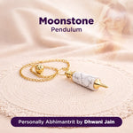 Moonstone pendulum with gold chain on a soft fabric background, branded as 'Personally Abhimantrit by Dhwani Jain'.