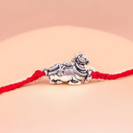 Silver bull charm on a red string against a beige background