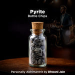 Glass bottle with cork lid containing pyrite chips, with a blurred background of a speaker at an event.