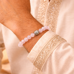 Close-up of a wrist wearing a pink beaded bracelet with a silver clasp on a person in an embroidered outfit.