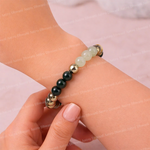 Bracelet with black, gold, and light green beads on a wrist against a neutral background