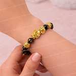 Gold and black beaded bracelet on a wrist against a light pink background