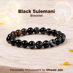 Black Sulemani bracelet on a light wooden surface with decorative elements.