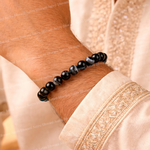 Black beaded bracelet on a wrist with a light pink fabric background