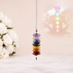 Colorful chakra beaded hanging ornament with a blurred background of flowers and a statue.