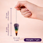 Hand holding a chakra pendulum with measurements on a beige background