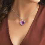 Necklace with a heart-shaped purple pendant worn by a person in a brown top.