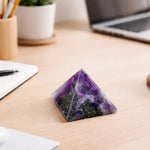Pyramid-shaped purple crystal on a desk with a laptop and office supplies in the background