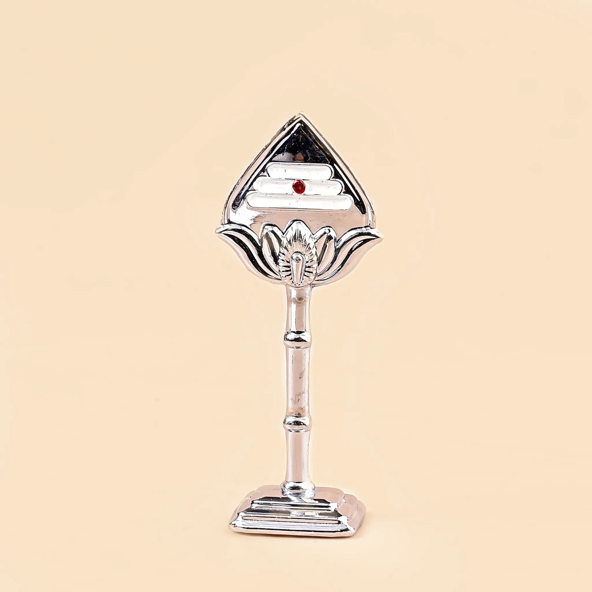 Decorative silver object with a red gemstone on a beige background