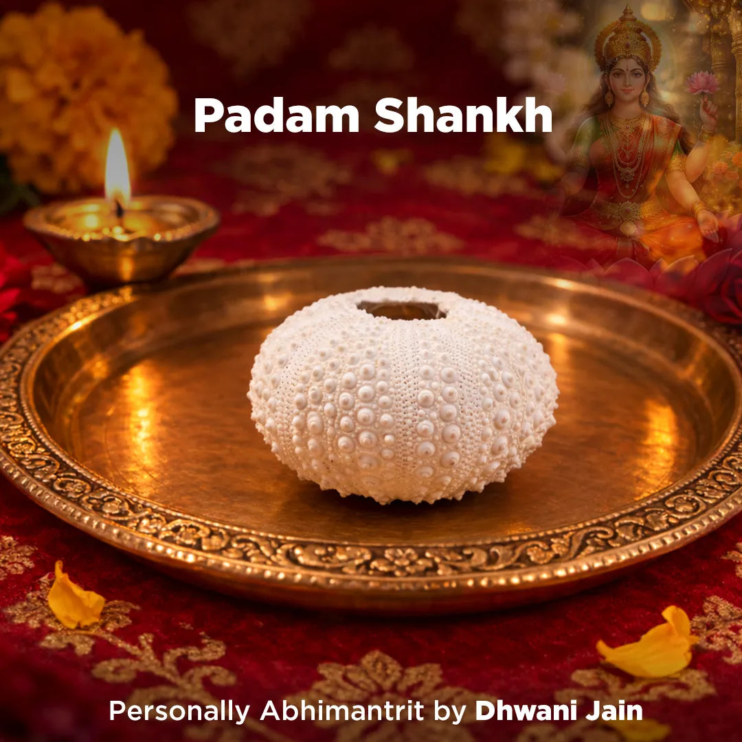 Decorative setting with a white shell on a gold plate, lit lamp, and figurine on a red fabric background.