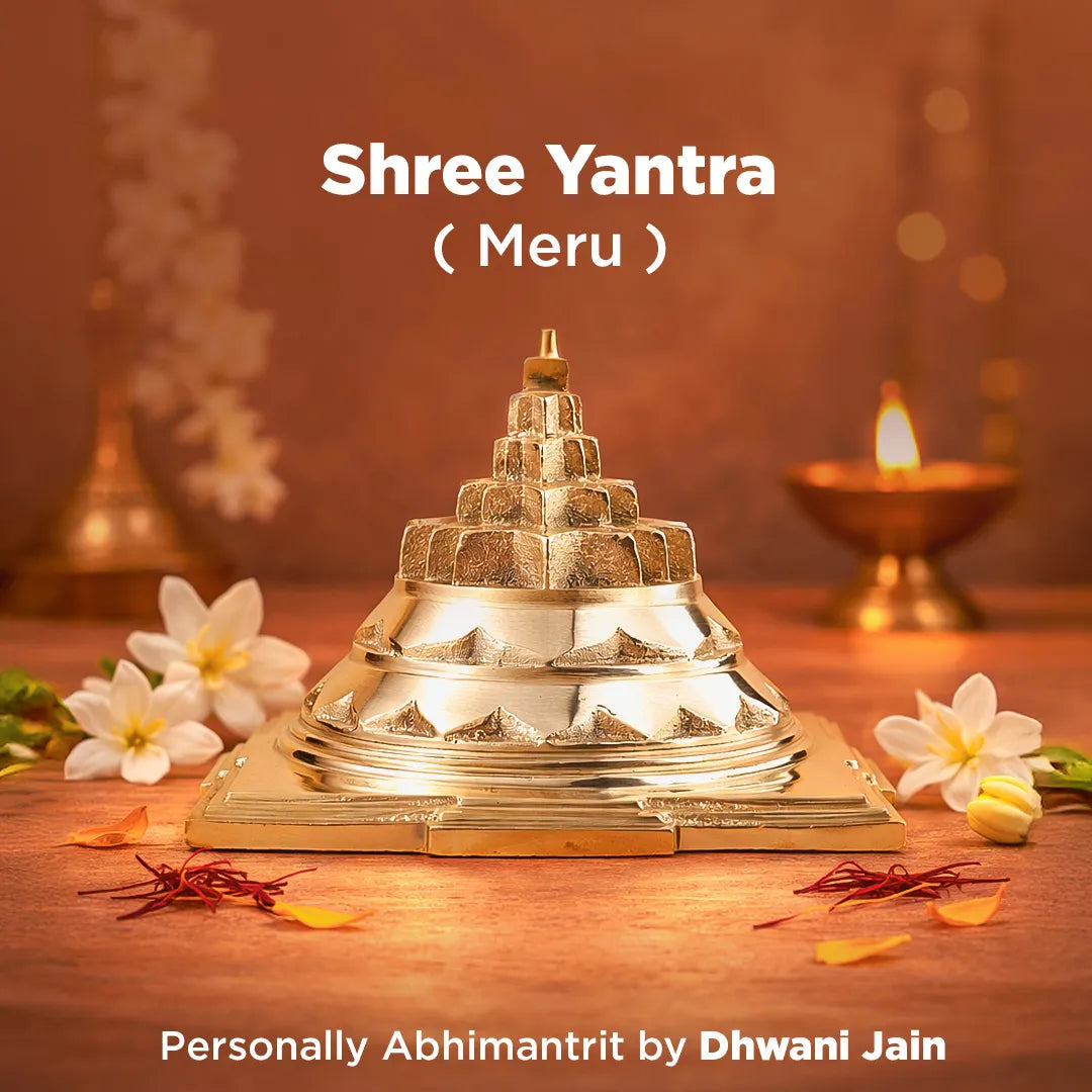 Shree Yantra Meru on a wooden surface with flowers and a lamp in the background