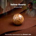 Yellow Quartz crystal ball on a reflective surface with people in the background