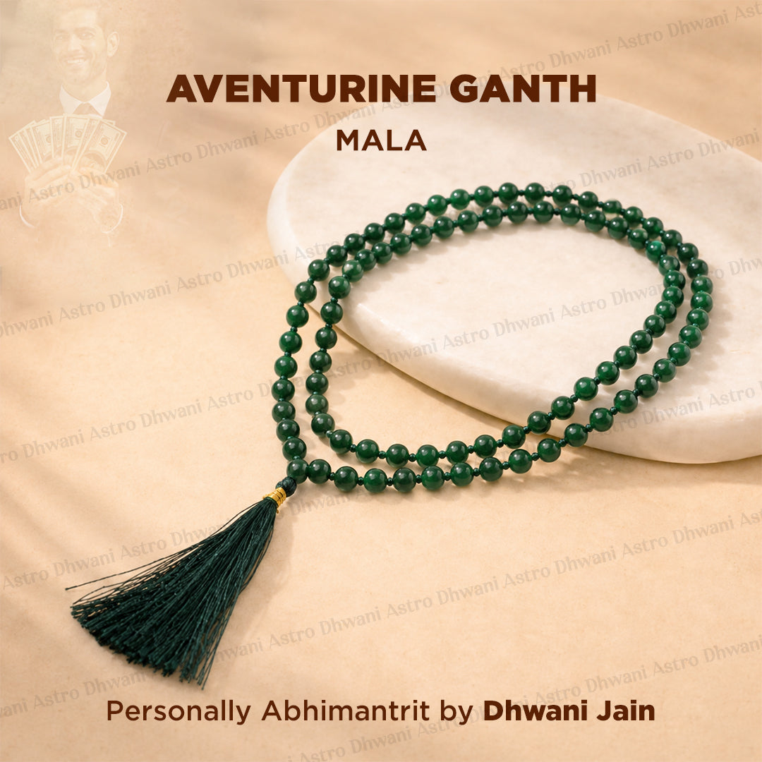 A green beaded mala necklace with a dark green tassel, displayed on a white stone slab over a beige fabric background.