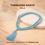A turquoise mala prayer bead necklace with a matching tassel, displayed on a white stone slab over a beige fabric background.