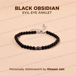 A black obsidian evil eye anklet bracelet displayed on a light peach background with text overlays. The bracelet consists of glossy black beads, a central evil eye motif with blue and white, and a silver-tone clasp.