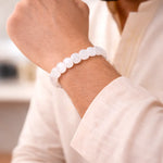 Close-up of a person wearing a white beaded bracelet on a blurred indoor background
