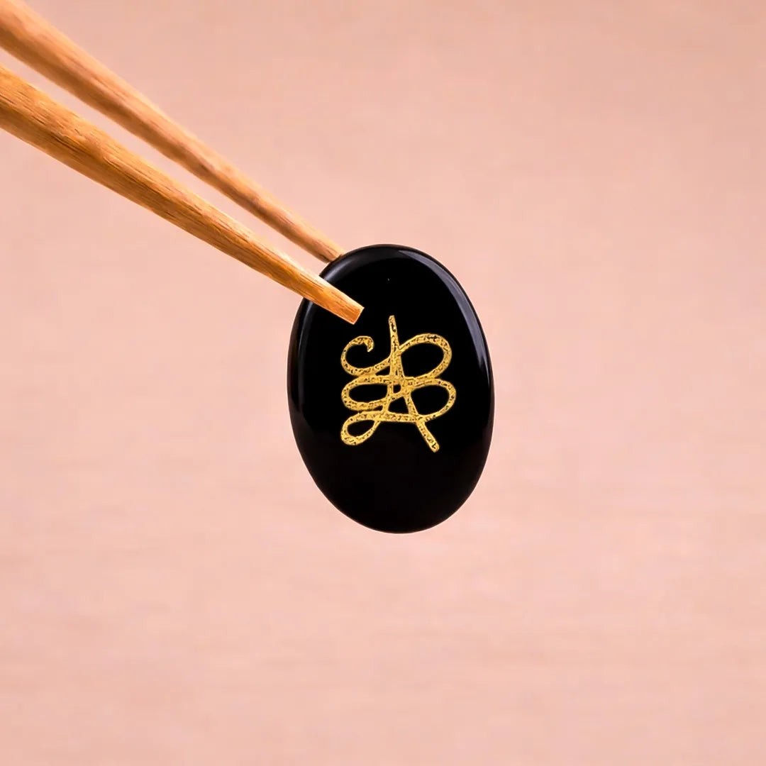 Black stone with gold emblem held by wooden chopsticks on a peach background