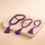 Purple beaded necklace with tassels on a stone surface