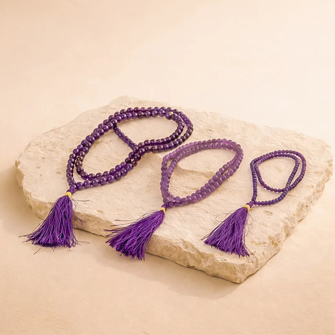 Purple beaded necklace with tassels on a stone surfaceAmethyst Crystal Mala – Peace, Focus & Spiritual Healing