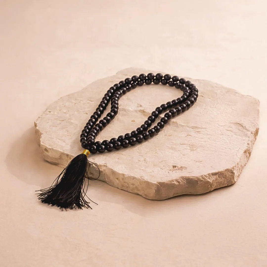 Black beaded necklace with a tassel on a stone surface