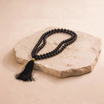 Black beaded necklace with a tassel on a stone surface