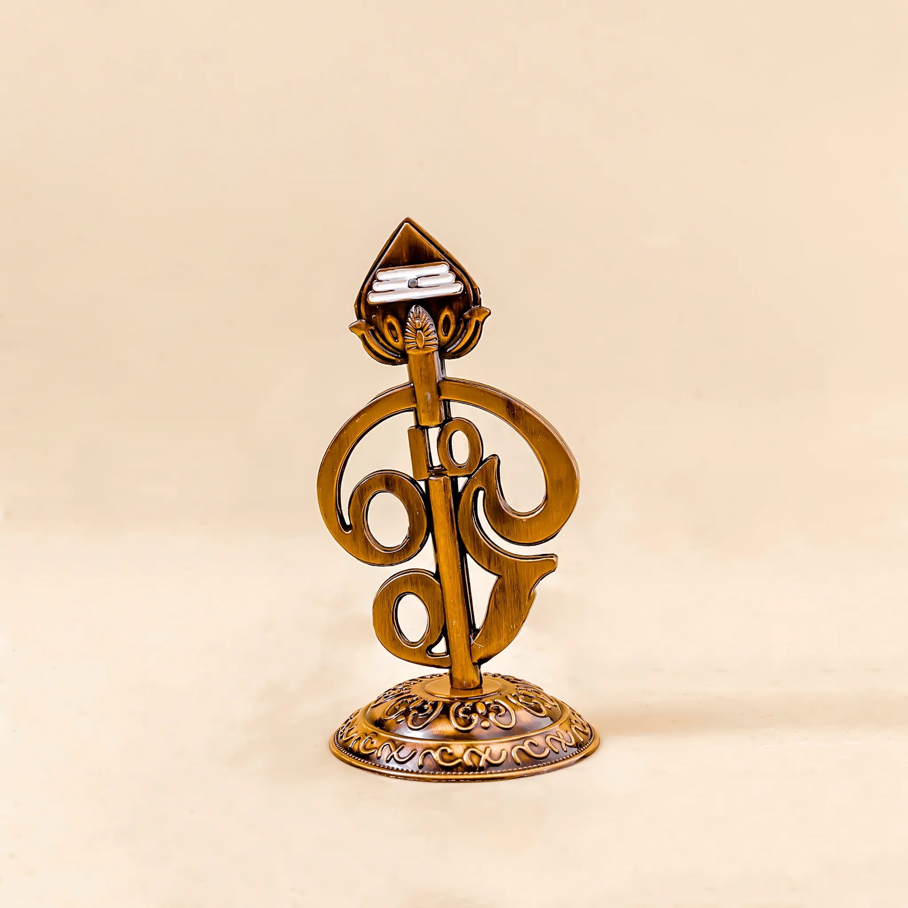 Decorative gold object with intricate design on a beige backgroundOm Vel – Divine Protection Symbol | Abhimantrit & Certified