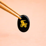 Black stone with gold deer engraving held by chopsticks on a peach background