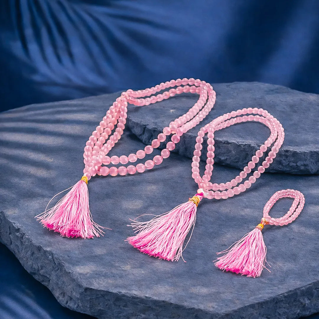 Pink beaded necklace with tassels on a dark stone surfaceRose Quartz Crystal Mala – Love, Peace & Emotional Healing