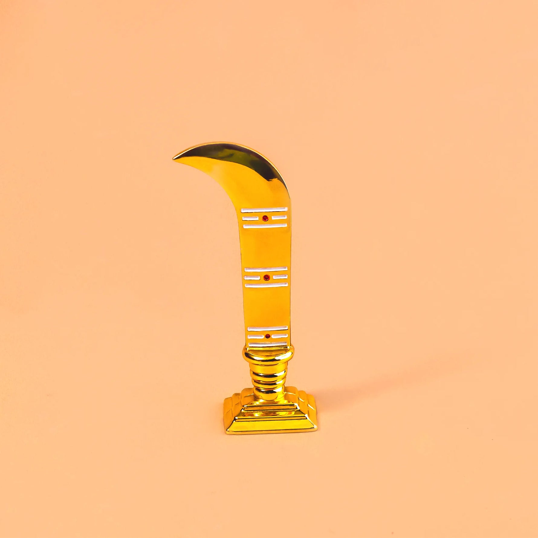 Decorative item resembling a gold sickle on a peach backgroundKaruwar Talwar Gold Plating – Divine Protection & Warrior Energy Symbol