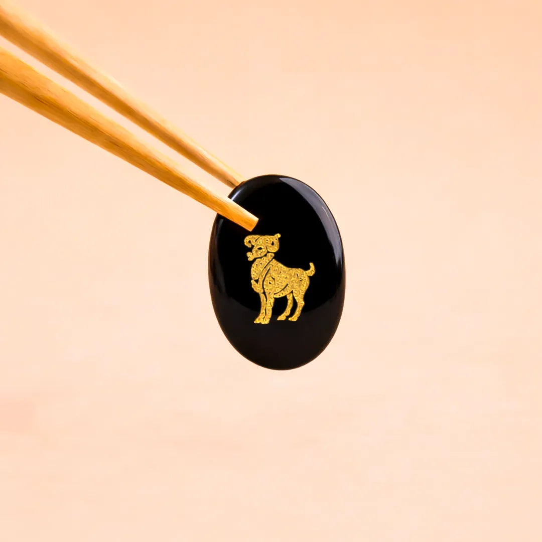 Black stone with gold dog engraving held by chopsticks on a beige backgroundAries Zodiac Sign Coin – Abhimantrit Astrology Coin for Courage & Energy