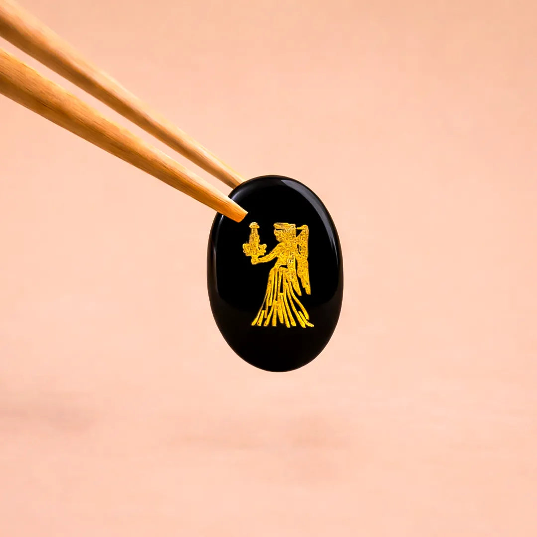 Black stone with gold angel design held by chopsticks on a peach background
