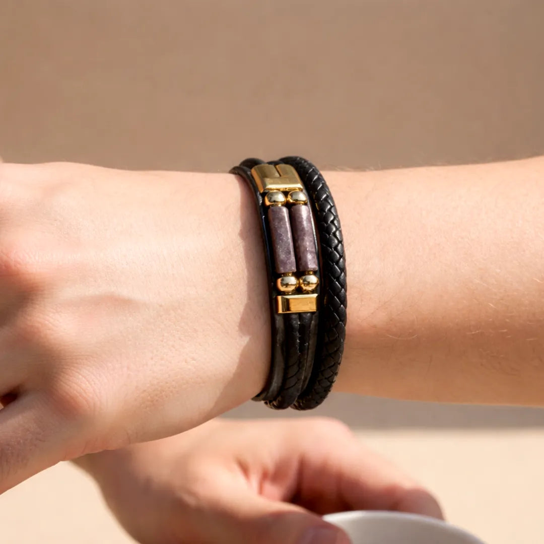 Close-up of a wrist wearing a black leather bracelet with gold accents on a beige background