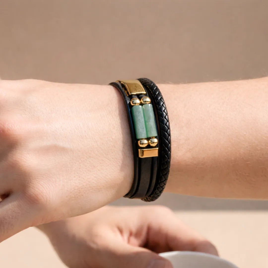 Close-up of a wrist wearing a black leather bracelet with green stones and gold accents against a beige background.Green Aventurine Leather Bracelet – Growth Energy & Positive Path Wear