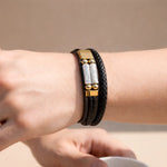 Black leather bracelet with gold accents on a wrist against a beige background