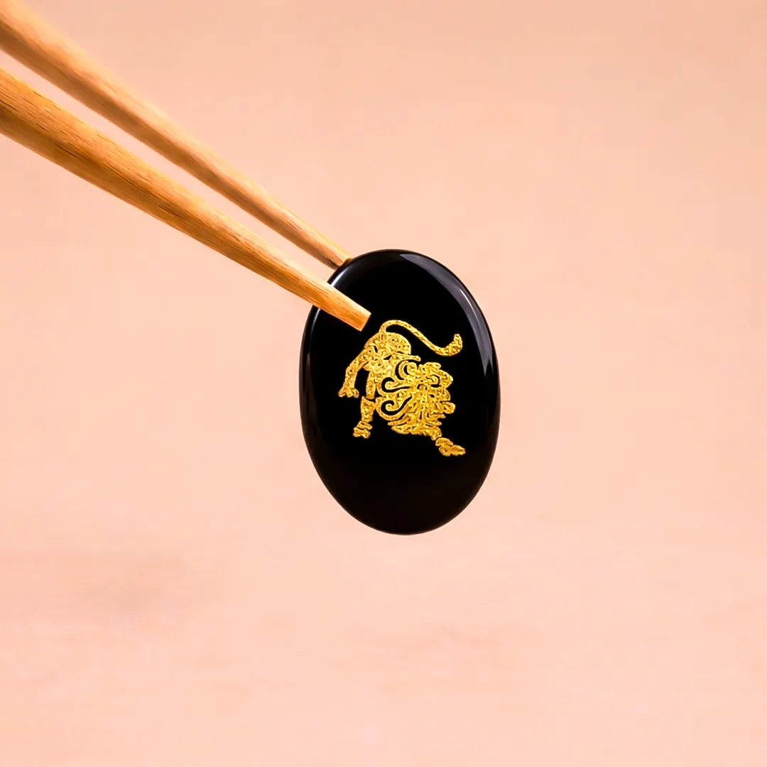 Black stone with gold lion design held by chopsticks on a beige background
