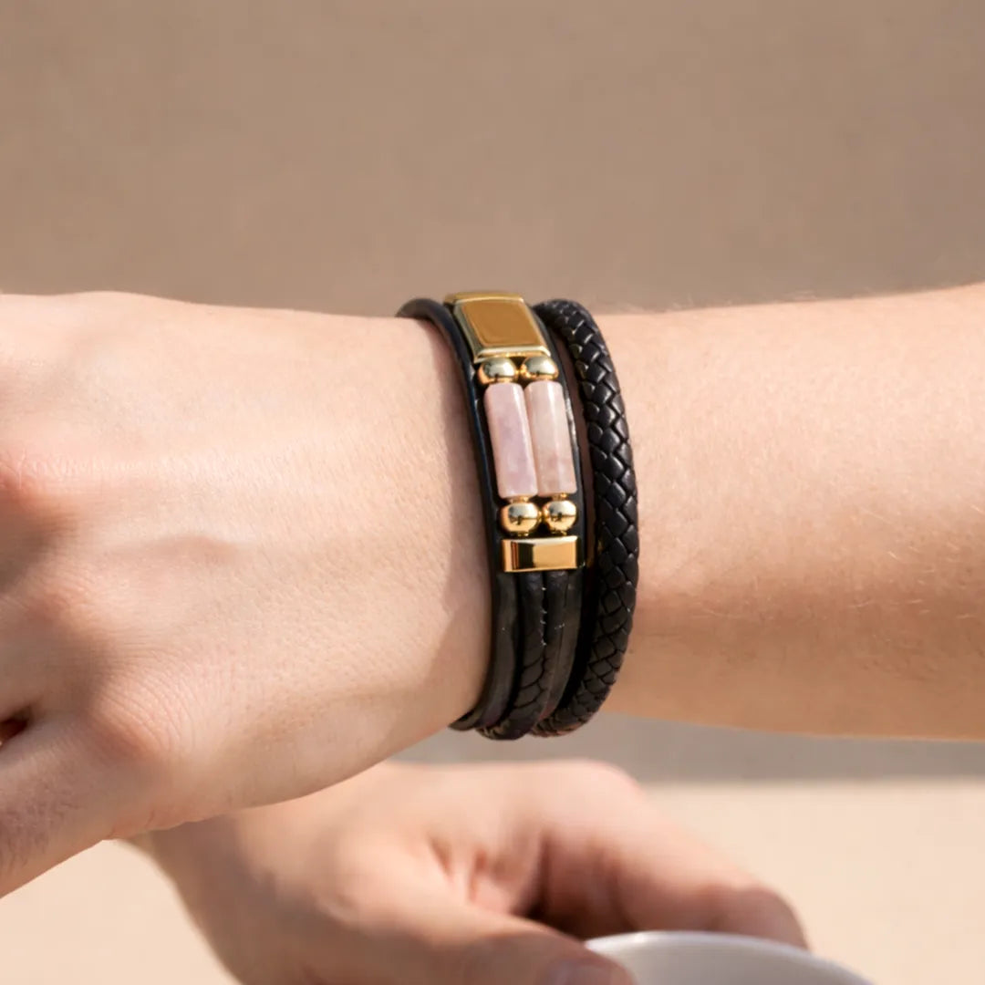 Close-up of a wrist wearing a black leather bracelet with gold accents on a beige background