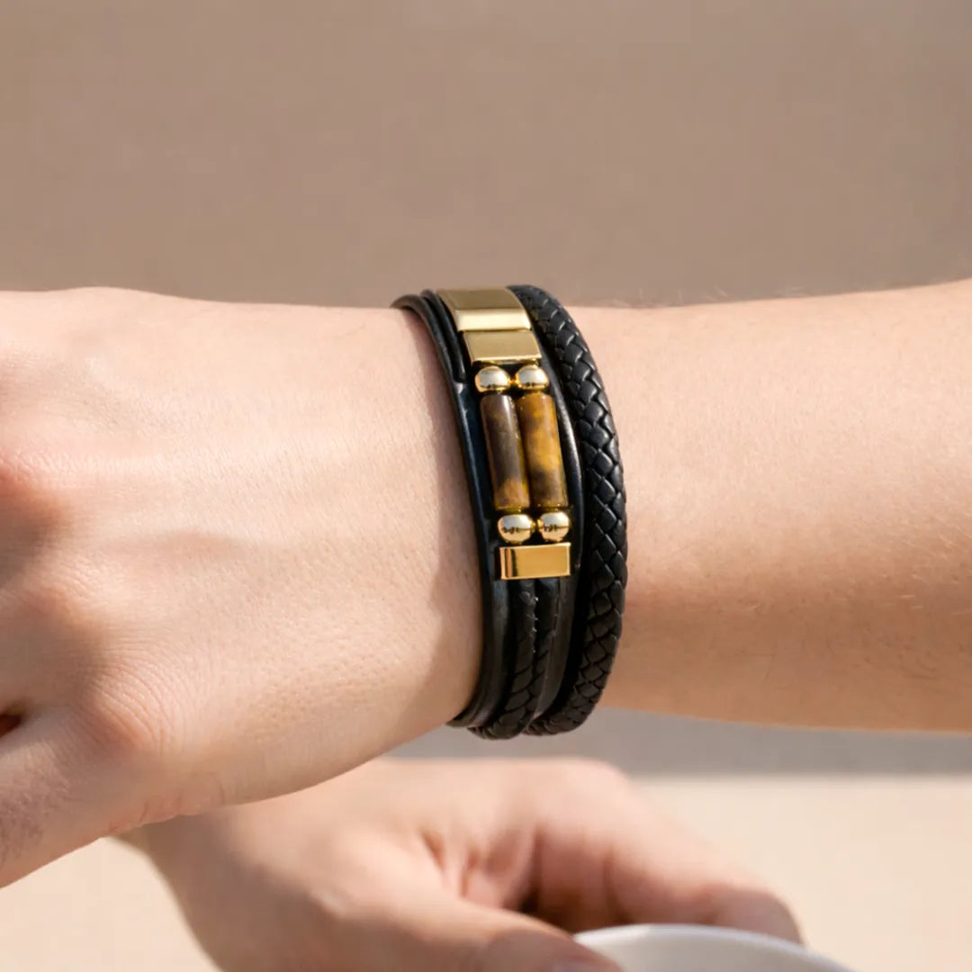 Close-up of a wrist wearing a black leather bracelet with gold accents on a neutral background