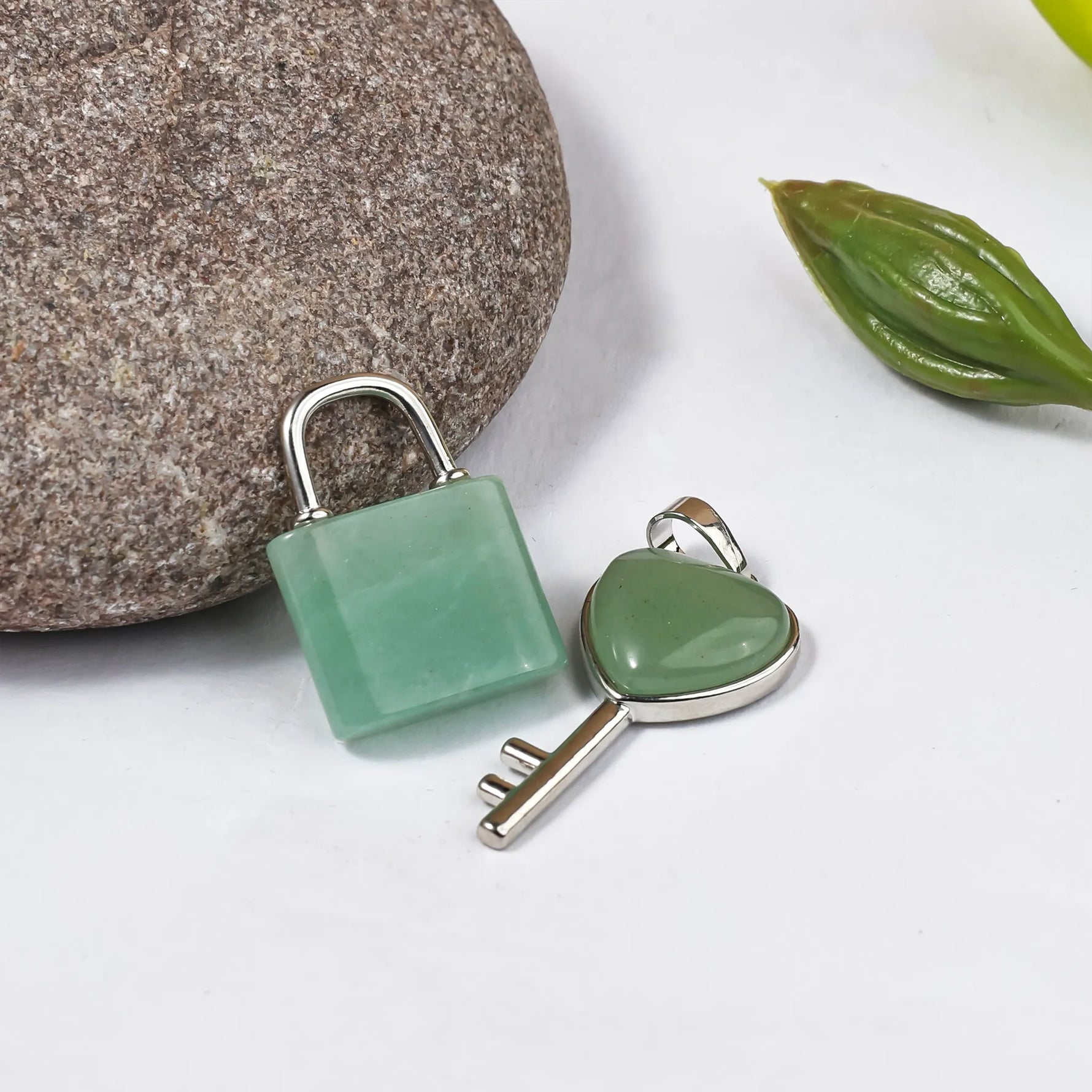 Green stone lock and key pendants on a white background with a stone and leaf.Green Aventurine Lock And Key Pendant - Abhimantrit & Certified