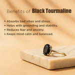 Gold ring with black gemstone on a beige surface, with text about black tourmaline benefits.