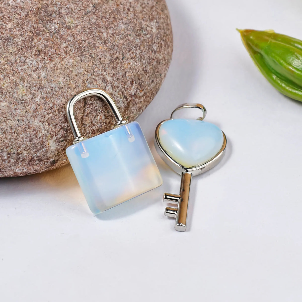 Opalite lock and key pendants on a white surface with a stone and leaf in the background.