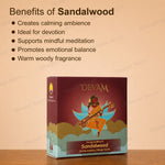 A boxed fragrance product labeled DEVAM Sandalwood sits on a wooden surface against a warm beige background with text listing benefits of sandalwood. The box is dark reddish brown with gold lettering and an illustrated figure playing a stringed instrument, with blue-green clouds at the bottom.